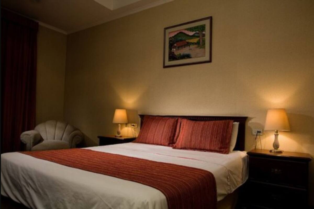 A hotel room with a bed, two bedside lamps, a chair, and a painting on the wall.