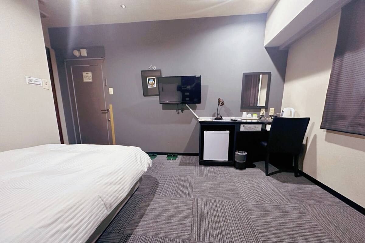 A hotel room with a bed, a desk, a small fridge, a TV, and a mirror.