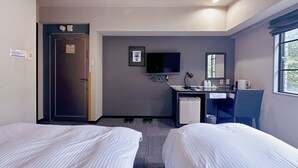 Una habitación de hotel con dos camas, un escritorio con computadora, televisión y ventana.