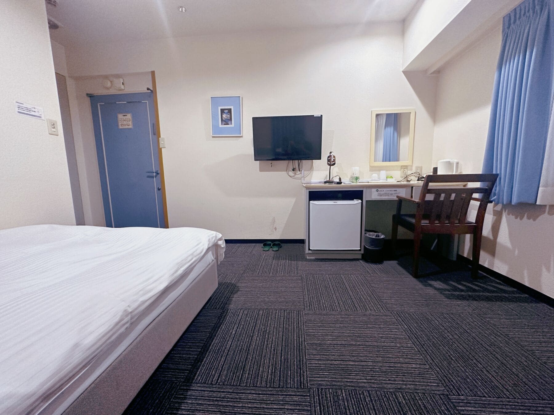 A hotel room with a bed, a desk with a computer, a television, and a small refrigerator.