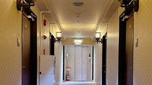 Un pasillo de hotel con piso alfombrado, luminarias fijadas a la pared y puertas que dan a las habitaciones.