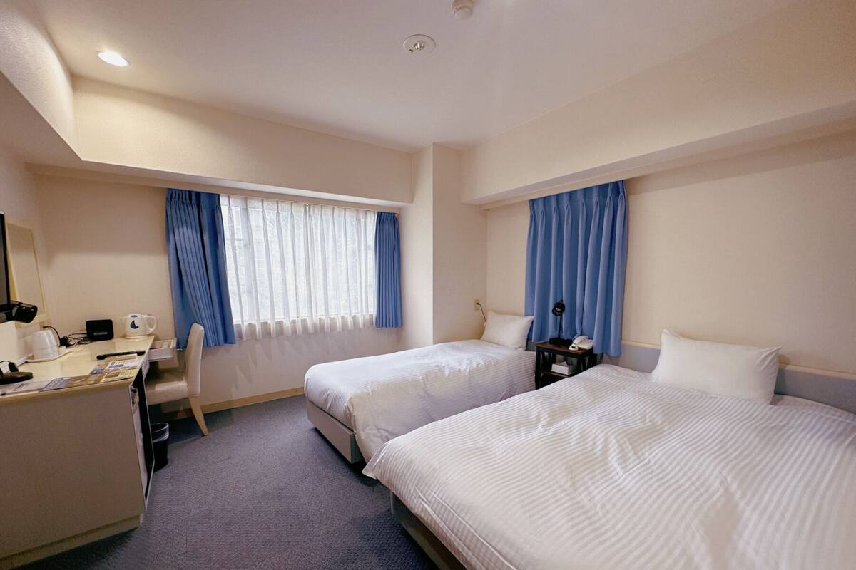 A hotel room with two beds, a desk, a chair, a telephone, and a window with curtains.
