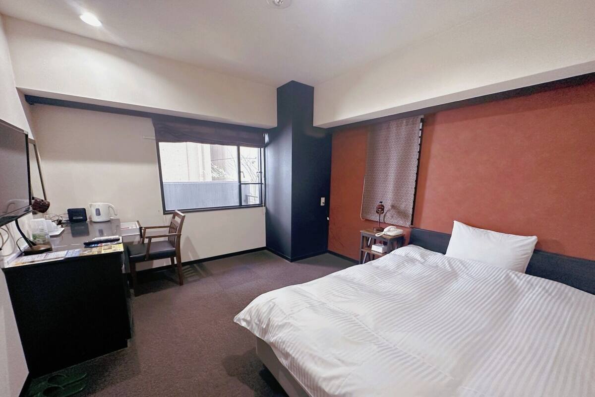 A hotel room with a bed, desk, chair, and a window.