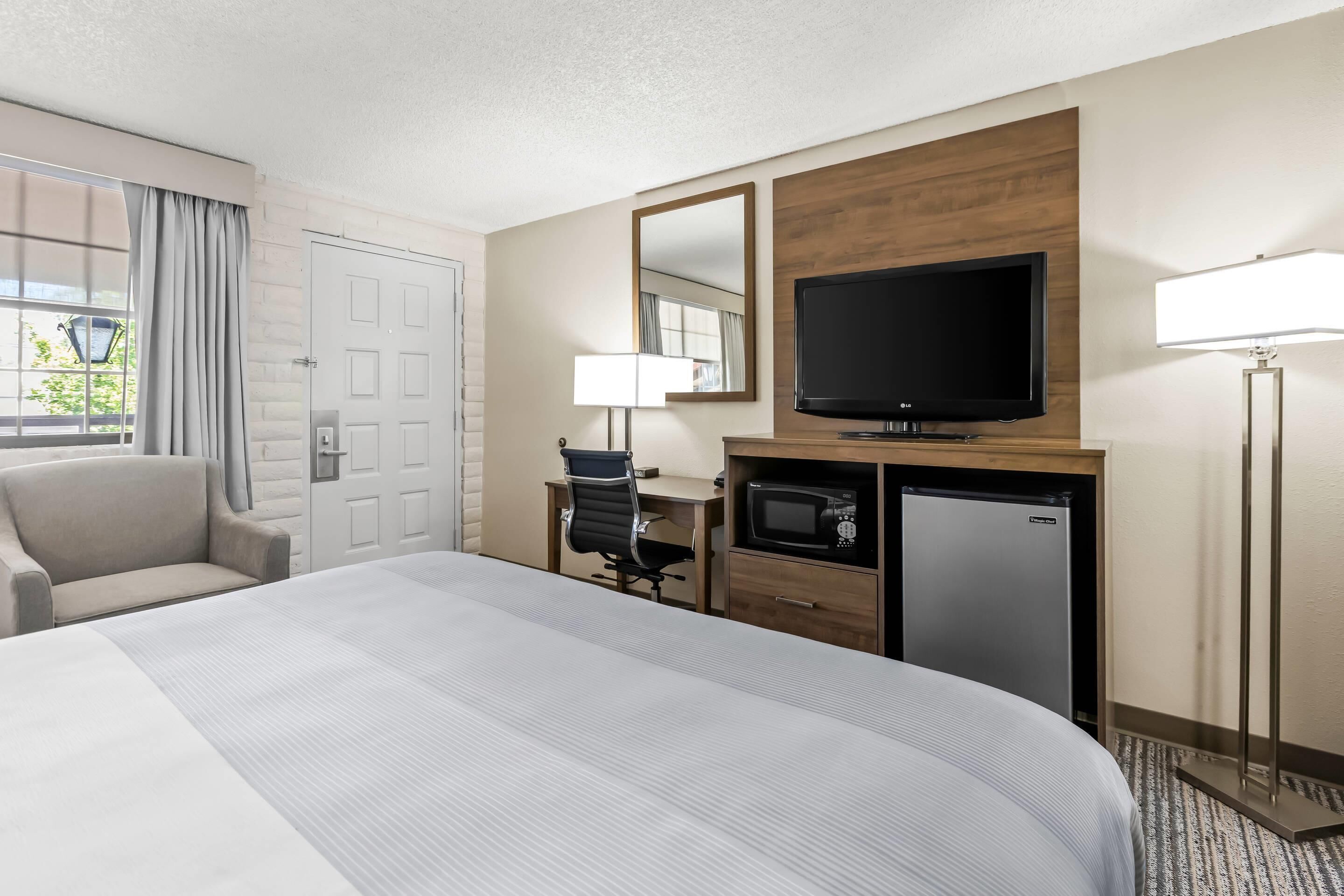 Een hotelkamer met een groot bed, een bureau met stoel, een televisie, een magnetron en een lamp.