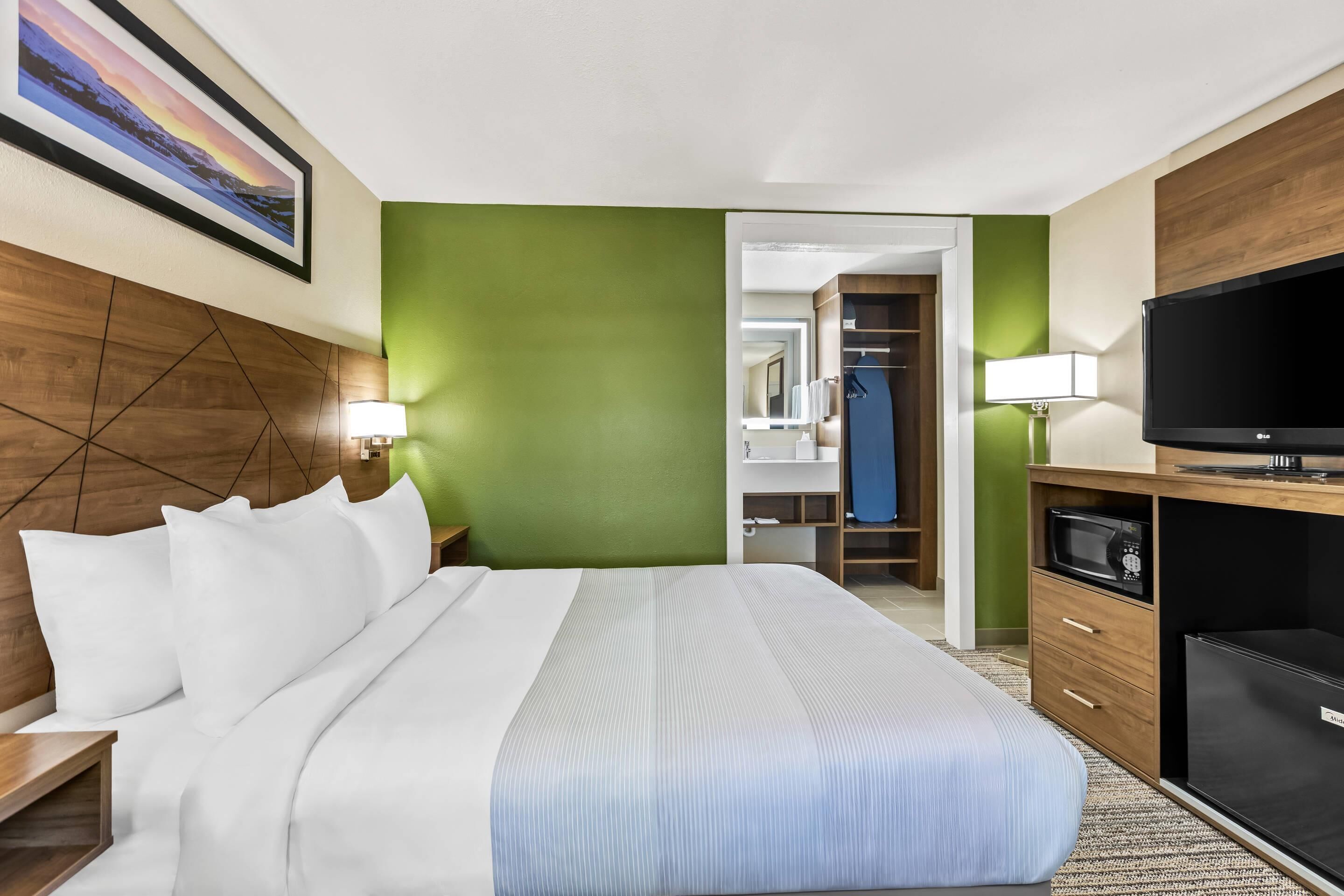 A hotel room with a large bed, a television, a wardrobe, and a bathroom visible through an open door.
