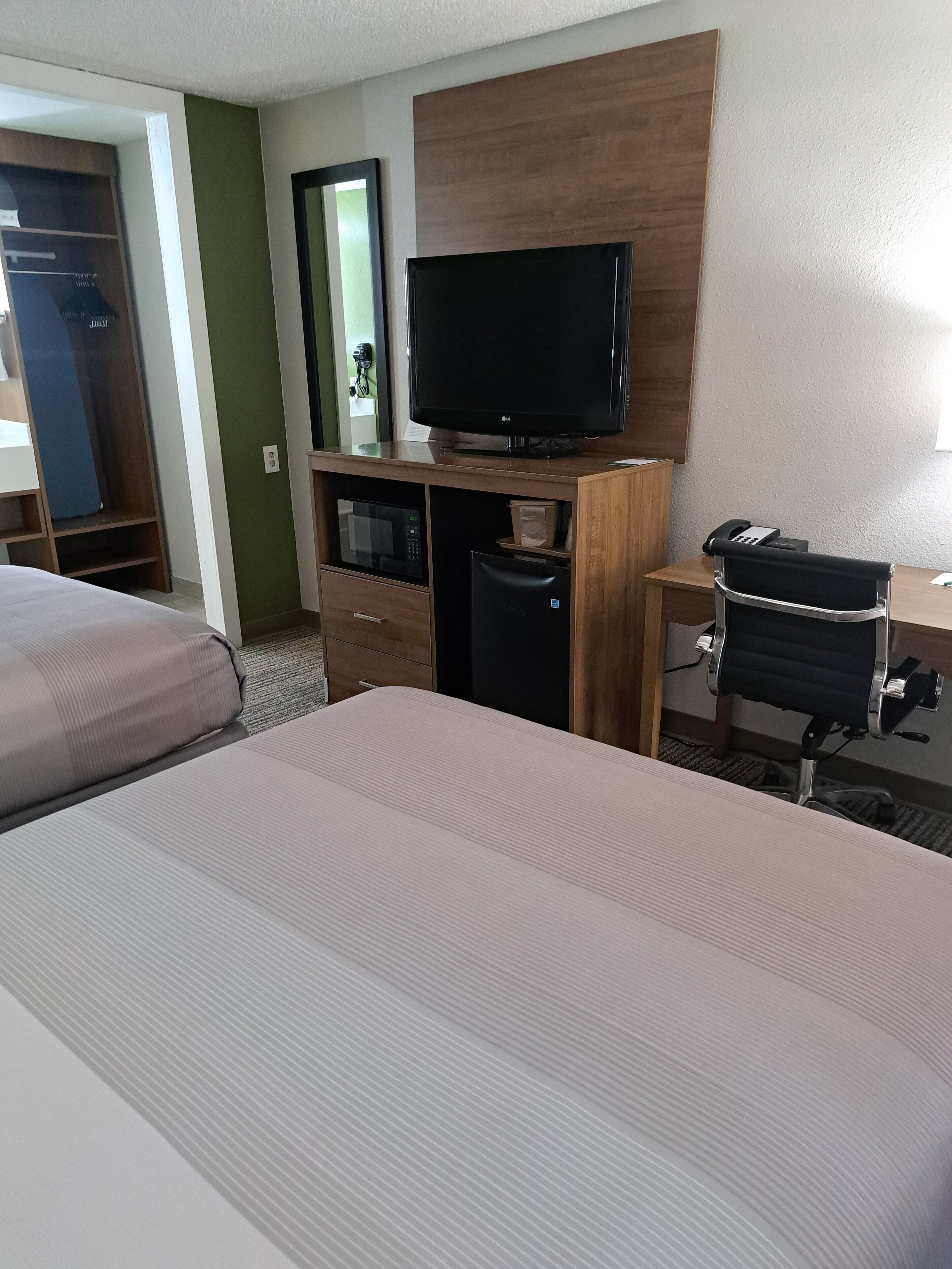 A hotel room with two beds, a desk with a chair, a television, a microwave, and a refrigerator.