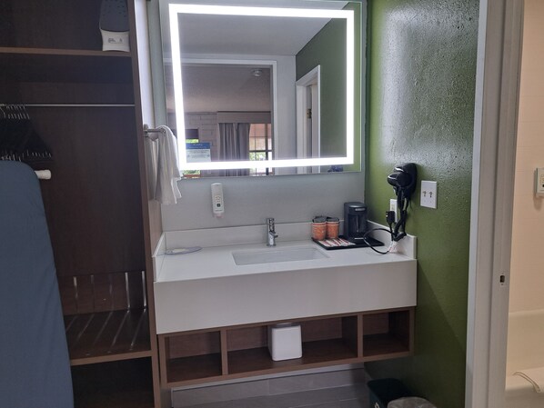 A hotel bathroom with a white sink, a mirror with built-in lighting, a hairdryer, and a coffee maker. - Quality Inn Baker City (Baker City)