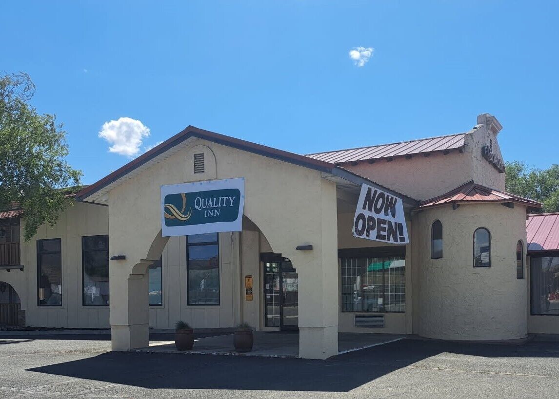 Un bâtiment sur lequel on peut lire une enseigne indiquant « Quality Inn » et une autre qui annonce : « OUVERT MAINTENANT ! ».