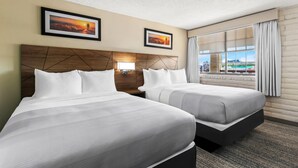A hotel room with two beds, a wooden headboard, a nightstand, a framed picture, and a window with curtains. - Quality Inn Baker City (Baker City)