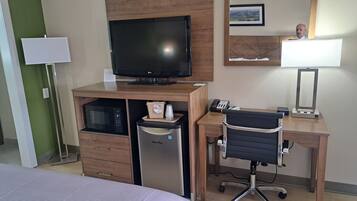 A hotel room with a bed, a desk with a computer, a television, a microwave, and a refrigerator.