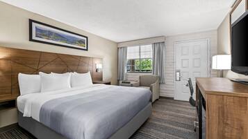 Ein Hotelzimmer mit einem großen Bett, einem Schreibtisch, einem Stuhl, einem Fernseher und einem Fenster mit Vorhängen.