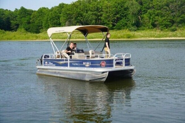 A small, open-air boat with a canopy, two people on board, and a calm water body with greenery in the background. - Honey Creek Resort (Moravia)