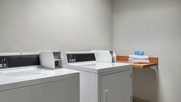 A laundry area with two front-loading washing machines and a wooden shelf with towels.