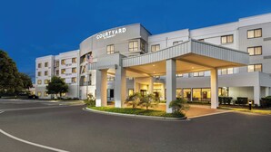 A Courtyard by Marriott hotel with a covered entrance, multiple floors, and a flag. - Courtyard by Marriott Burlington Mt. Holly Westampton (Mount Holly)