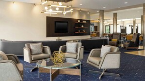 A modern lobby with a sofa area, a glass coffee table, and a mounted TV. - Courtyard by Marriott Burlington Mt. Holly Westampton (Mount Holly)