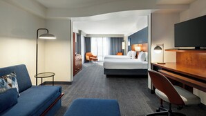 A hotel room with a sofa, a desk, a bed, a TV, and a view of the hallway. - Courtyard by Marriott Burlington Mt. Holly Westampton (Mount Holly)