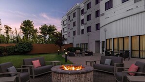 A circular stone fire pit surrounded by outdoor seating, with a building in the background. - Courtyard by Marriott Burlington Mt. Holly Westampton (Mount Holly)