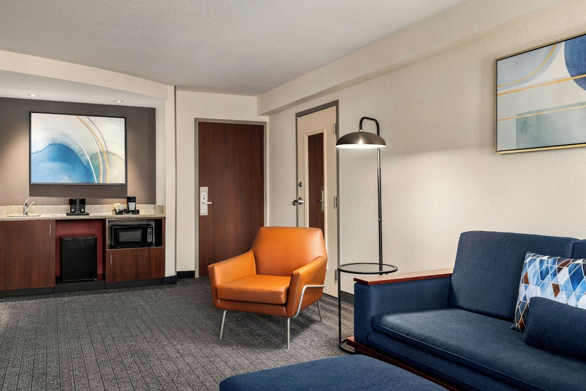 A hotel room with a kitchenette, a sofa, a chair, and a floor lamp.