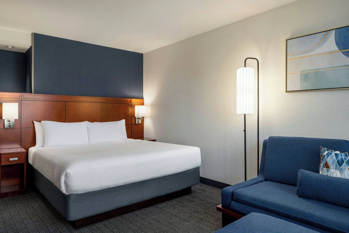 A hotel room with a large bed, a blue sofa, a nightstand, a lamp, and a painting on the wall.