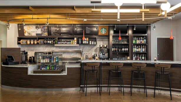 A modern bar area with a curved counter, bar stools, and a variety of beverages and snacks. - Courtyard by Marriott Burlington Mt. Holly Westampton (Mount Holly)