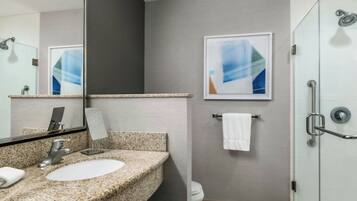 Un baño moderno con lavamanos de granito, un espejo grande, un cuadro abstracto enmarcado y cabina de ducha de vidrio.