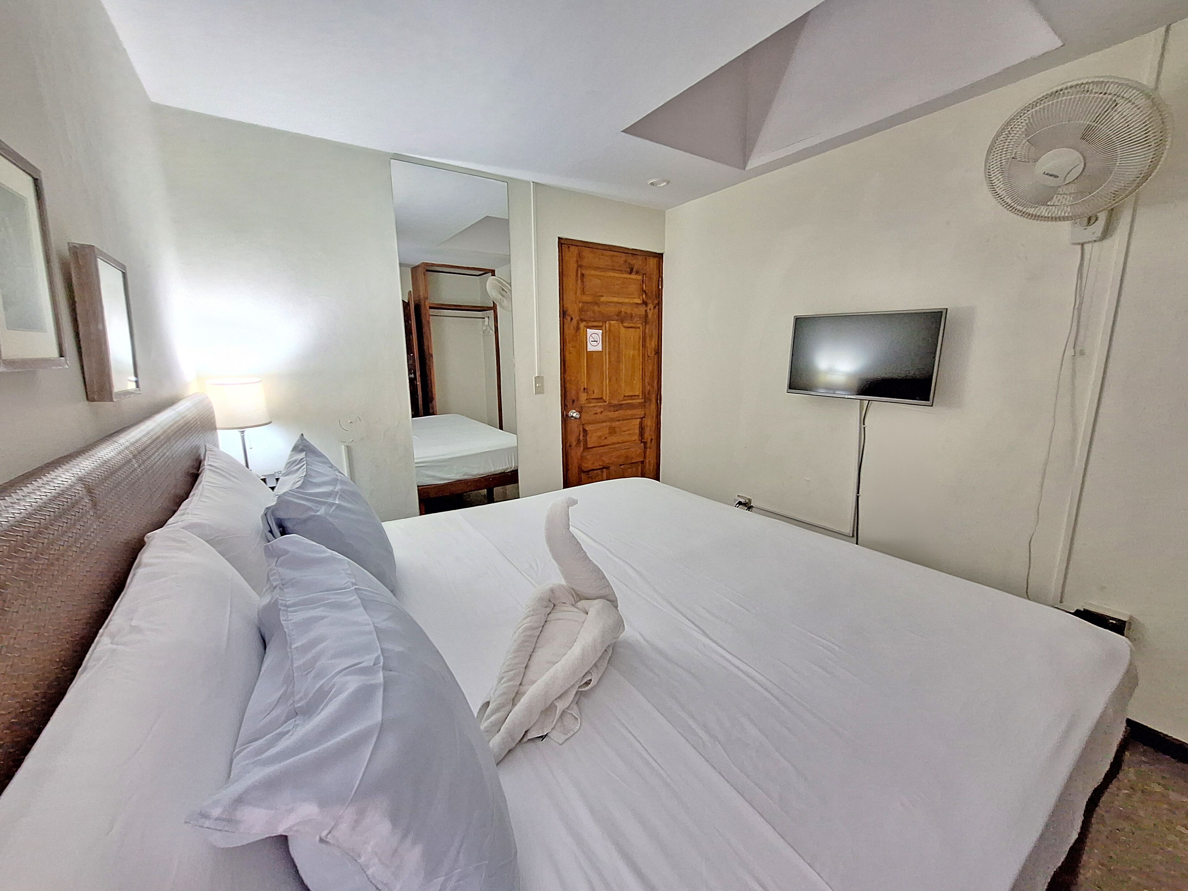 Ein Hotelzimmer mit einem Bett, einem Fernseher, einem Ventilator und einer Tür zu einem Badezimmer.