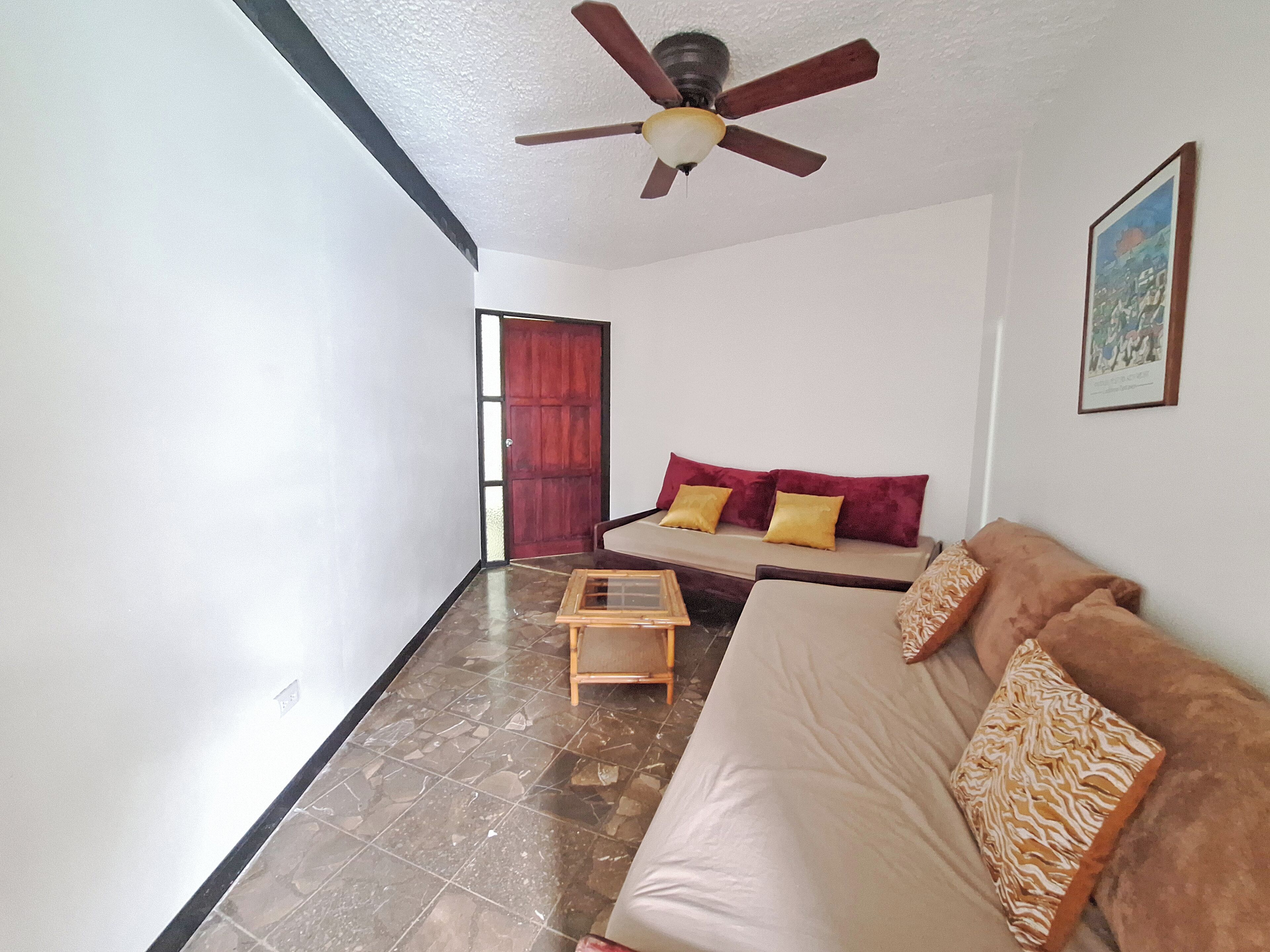 A living room with a sofa, a small table, a ceiling fan, and a door.