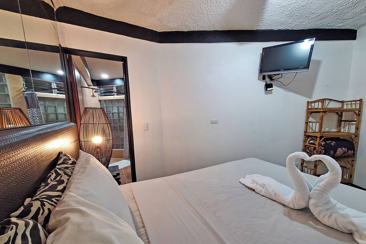Een hotelkamer met een bed, een aan de muur bevestigde televisie, een spiegel en een raam met gordijnen.