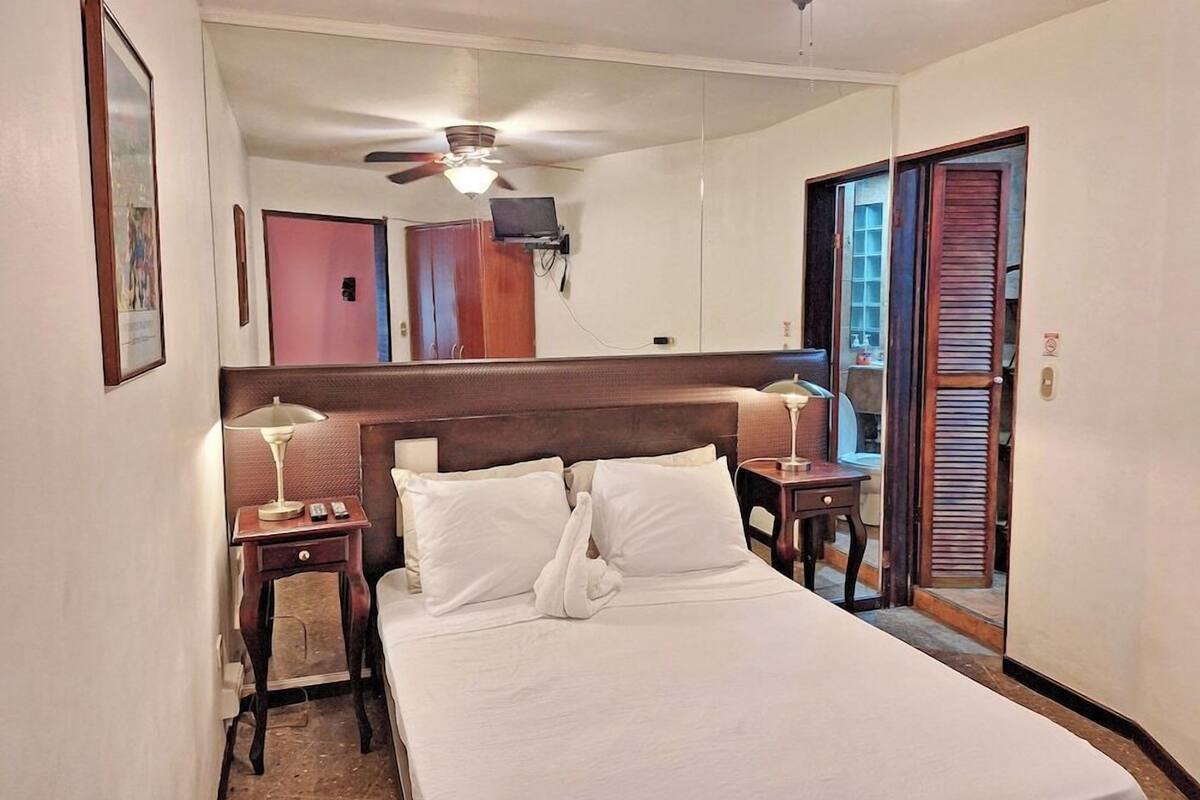 Een hotelkamer met een bed, twee nachtkastjes, een plafondventilator en een spiegel.