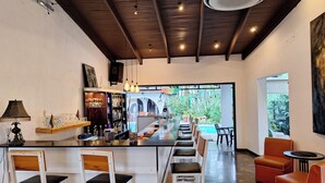 A bar area with a long counter, multiple bar stools, and a view of the outdoor patio. - Colours Oasis Resort ADULT ONLY (San José)