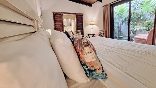 A hotel room with a large bed, a wooden ceiling, a bathroom with a mirror, and a view of greenery outside. - Colours Oasis Resort ADULT ONLY (San José)
