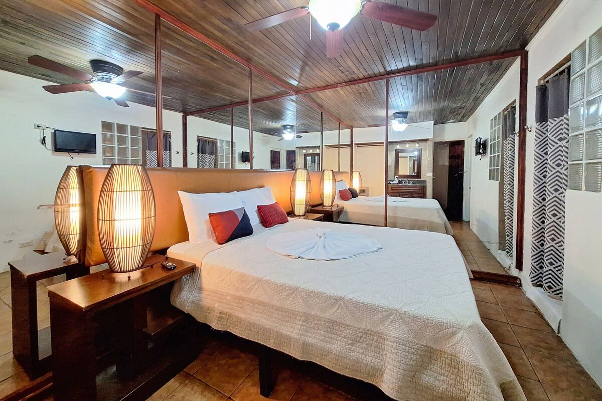 Een hotelkamer met een groot bed, houten plafond, plafondventilatoren en een televisie aan de muur.