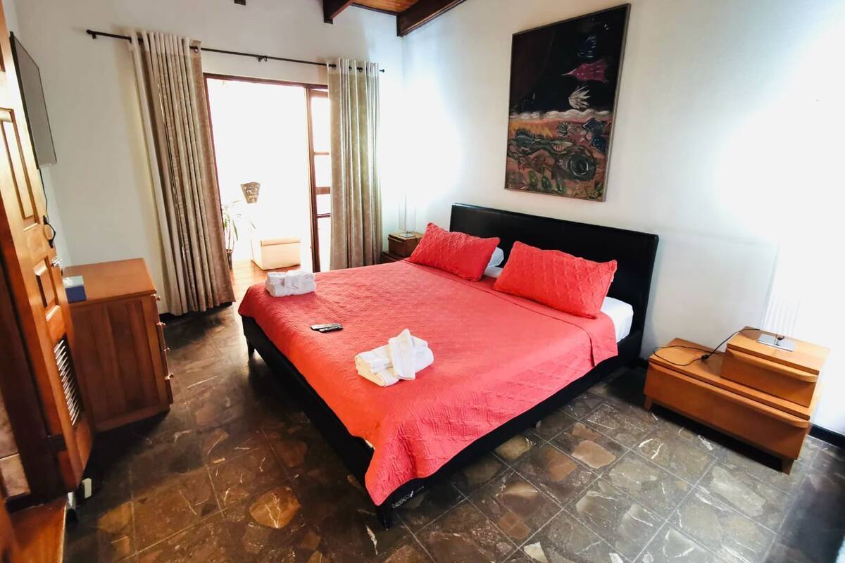 Een hotelkamer met een groot bed, houten hoofdeinde en een schilderij aan de muur.