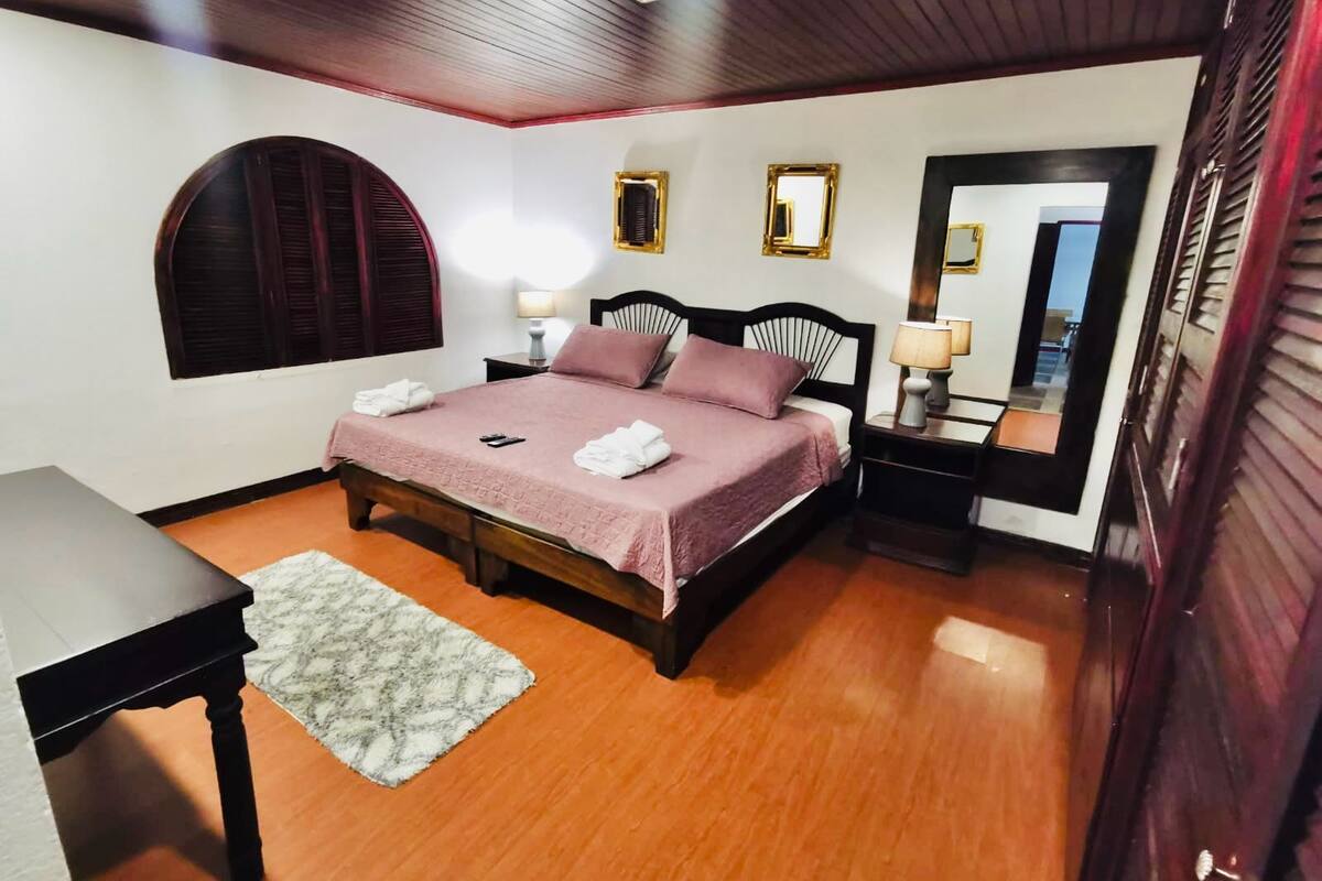 Een keurig opgemaakt slaapkamer met een bed, nachtkastjes, een spiegel en een klein tafeltje.