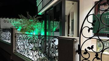 A hotel entrance with a decorative iron gate, a visible sign reading "GUESTS," and a green-lit exterior.