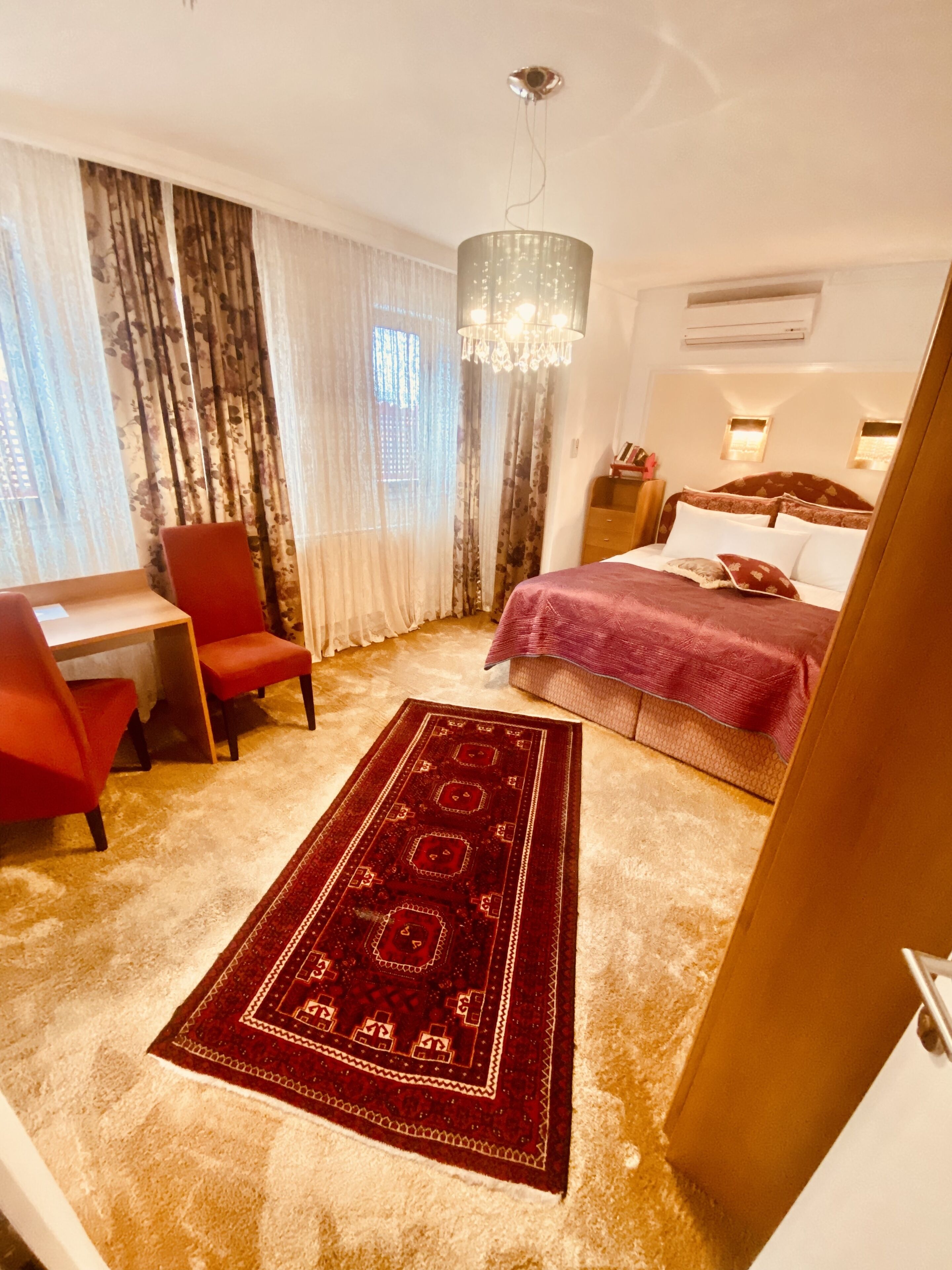 Habitación de hotel con cama, escritorio, silla, candelabro y una alfombra grande.