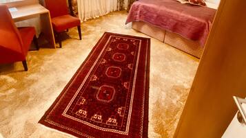 Habitación de hotel con cama, escritorio, silla, candelabro y una alfombra grande.