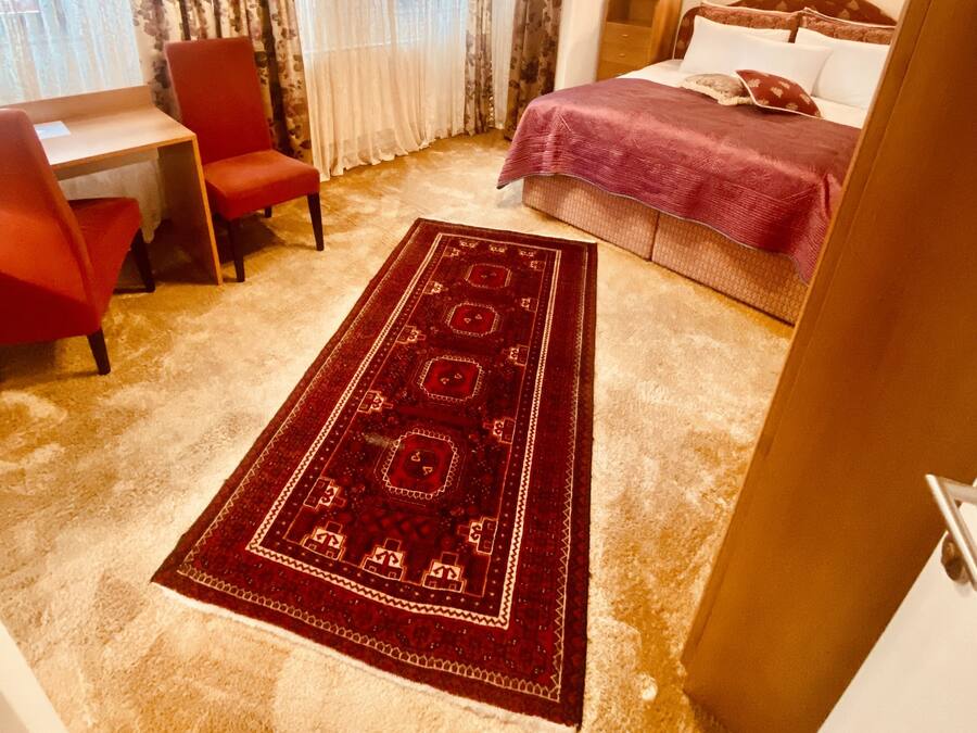 Habitación de hotel con cama, escritorio, silla, candelabro y una alfombra grande.