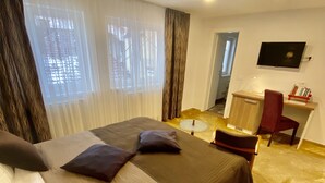 Une chambre d’hôtel avec deux lits, un bureau, une chaise, une télévision et une fenêtre avec des rideaux.