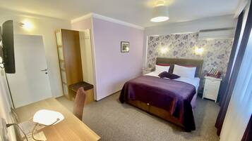 Quarto de hotel com cama, mesas de cabeceira, escrivaninha com abajur, cadeira, guarda-roupa e porta.