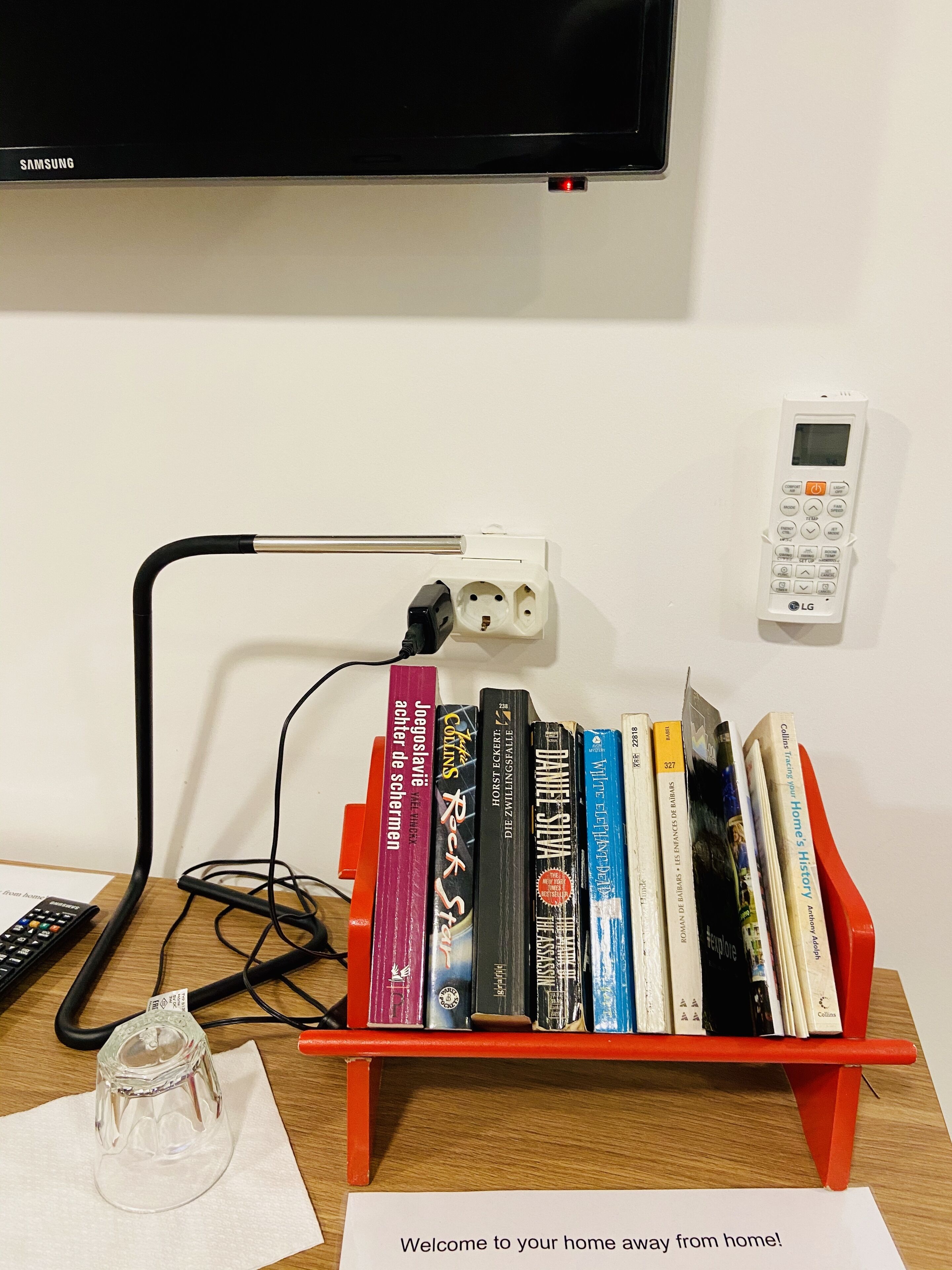 Une bibliothèque remplie de livres, une télécommande, un verre et un thermostat fixé au mur.