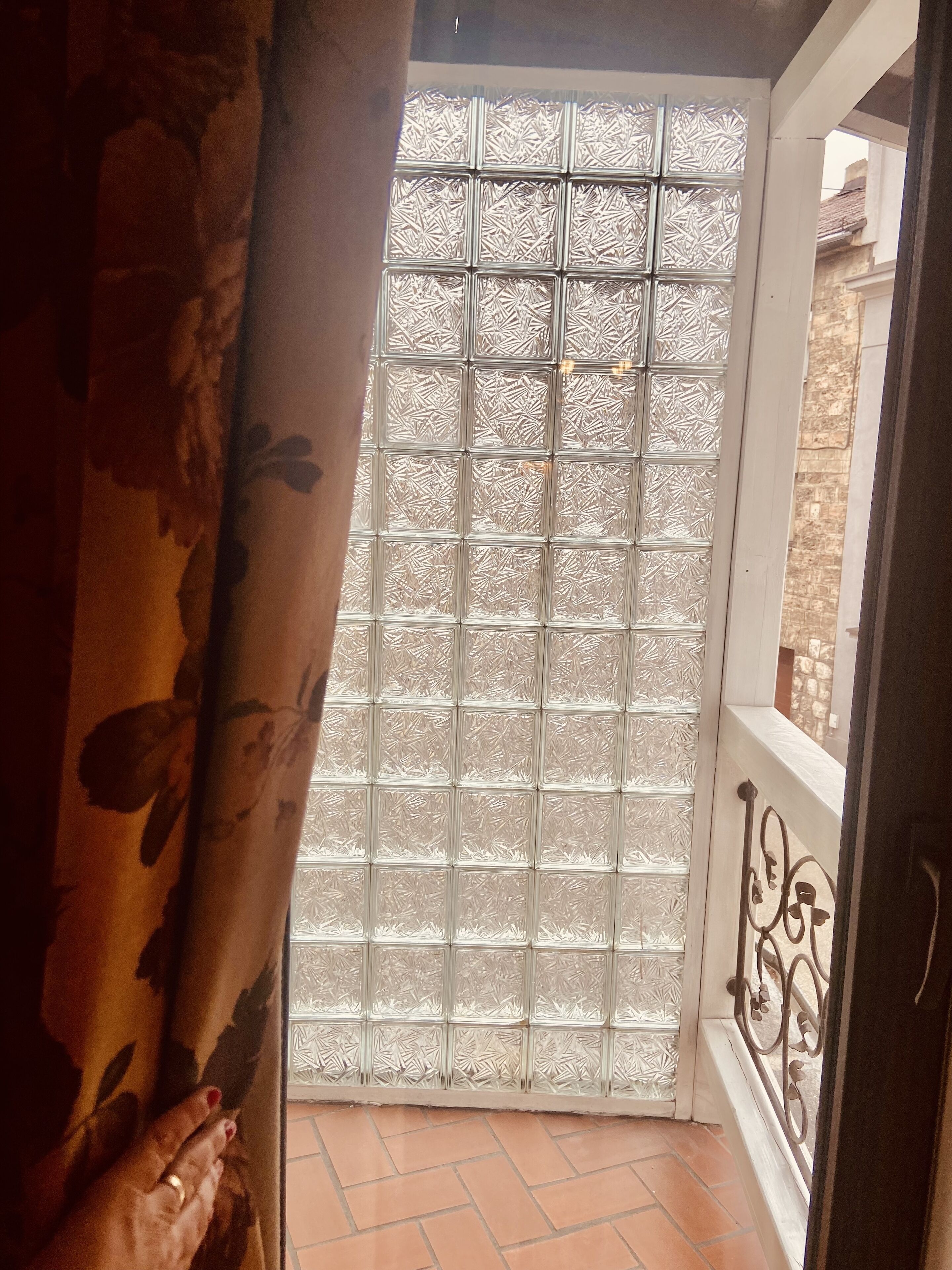 A balcony with a patterned glass door, a tiled floor, and a metal railing.