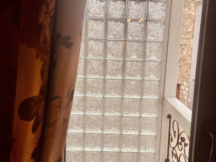 A balcony with a patterned glass door, a tiled floor, and a metal railing.