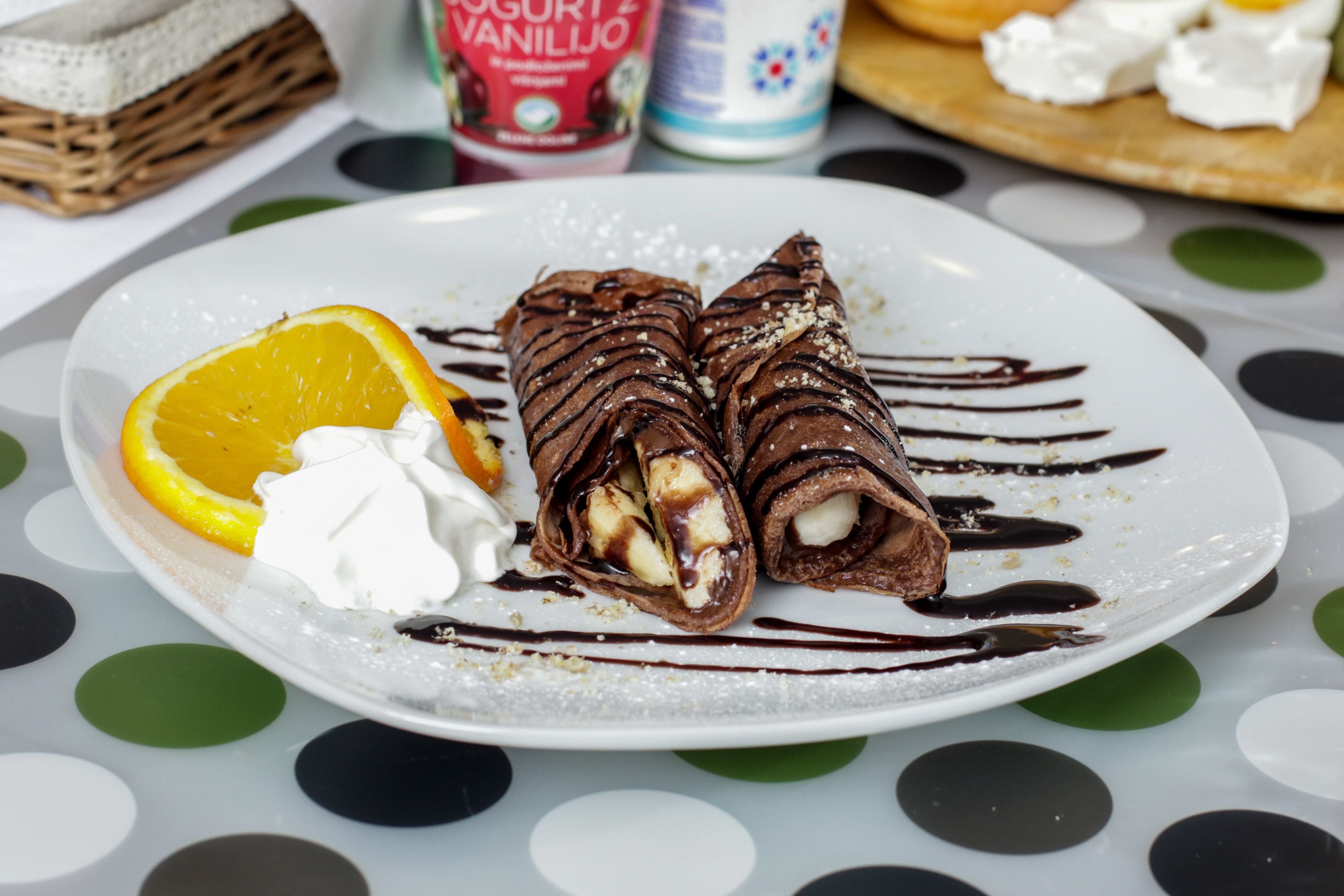 Um prato com rolinhos de chocolate, chantilly e uma fatia de laranja.