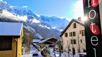 Un village de montagne enneigé, avec une enseigne d’hôtel, une voiture sur une route bordée de neige et des bâtiments à l’architecture traditionnelle.