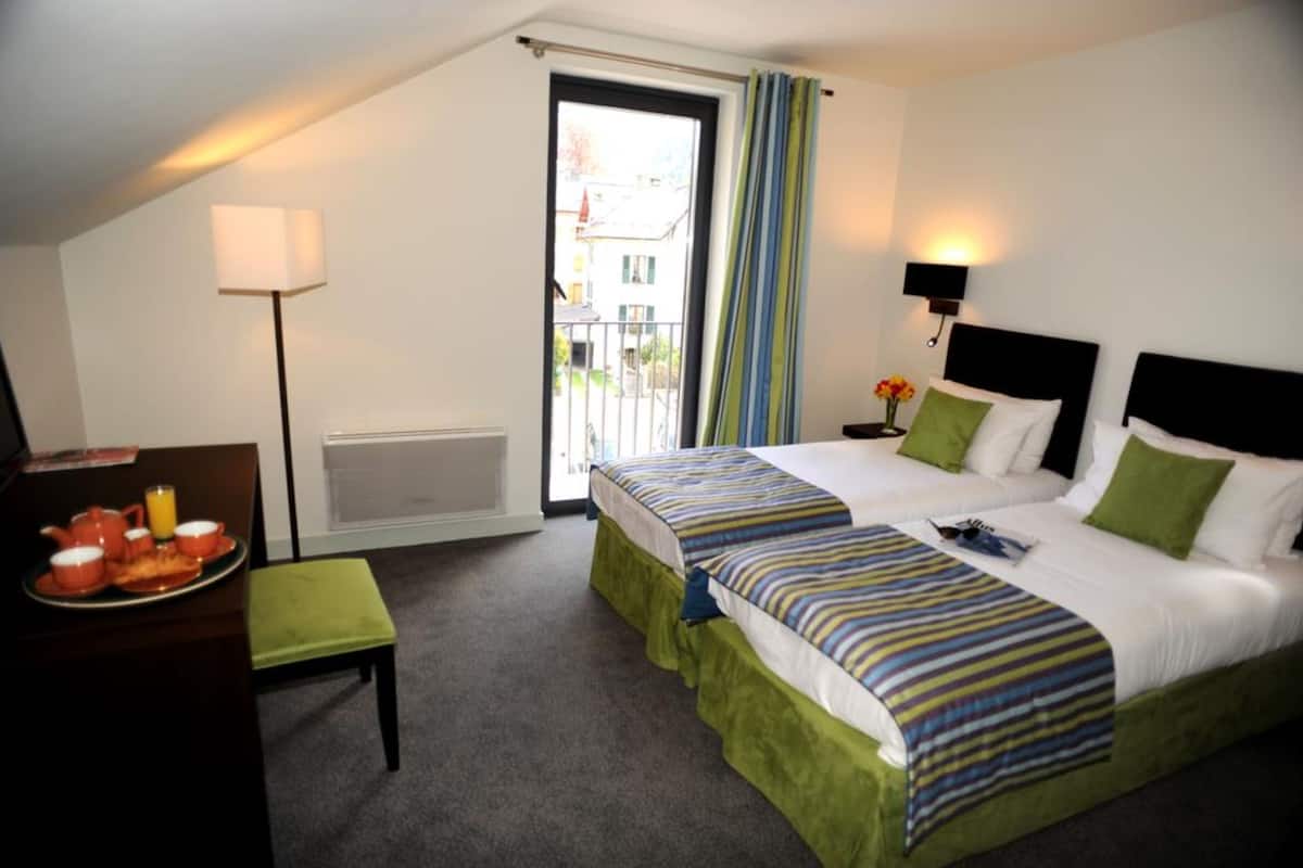 A hotel room with two beds, a dining table with breakfast, a lamp, and a view of the outside.