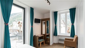 A hotel room with a bed, a desk with a chair, a TV, and a window with curtains. - Hotel Les Lanchers (Chamonix-Mont-Blanc)