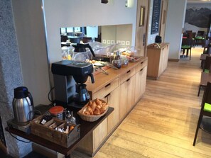 A breakfast bar with coffee machines, a bread basket, and a fruit bowl. - Hotel Les Lanchers (Chamonix-Mont-Blanc)