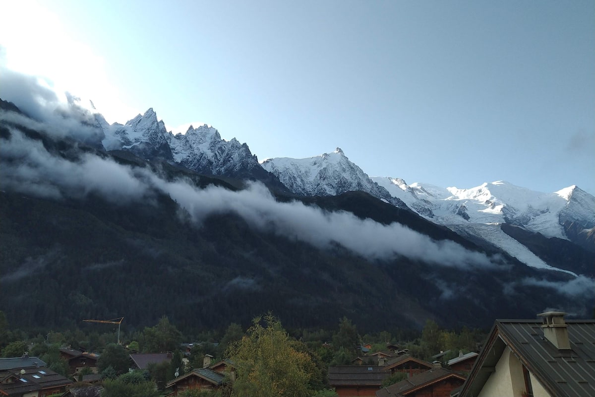 A mountain landscape with snow-capped peaks, a village with traditional houses, and a forested valley.