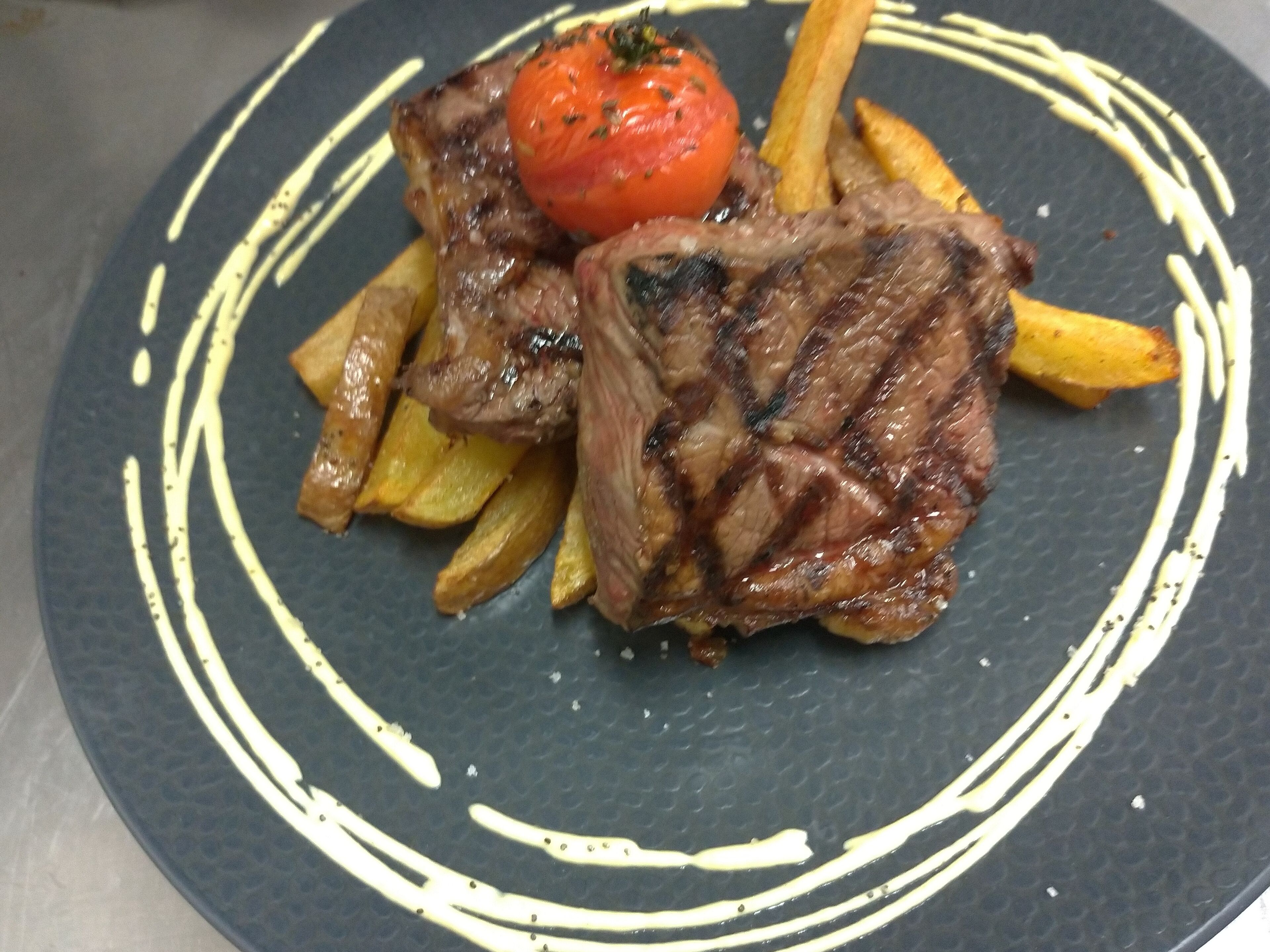 En tallerken med grillstegt kød, pommes frites og en tomatpynt.